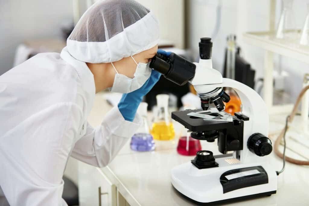 Young woman medical researcher looking through microscop slide in the life science (forensics, micro