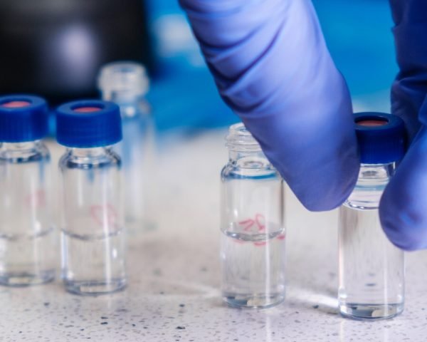 Close up scientist hand in rubber gloves takes a glass vial with a blue cap for HPLC analysis