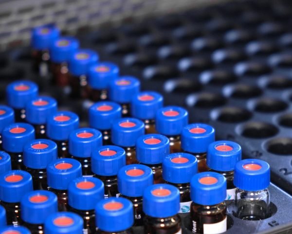 Glass vials with blue caps are in the rack of HPLC system with autosampler. Separation of compounds