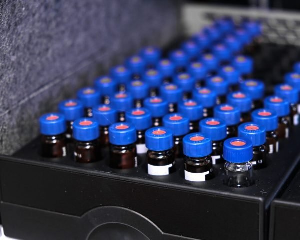 Glass vials with blue caps are in the rack of HPLC system with autosampler. Separation of compounds