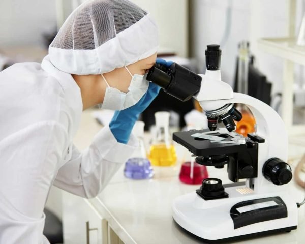 Young woman medical researcher looking through microscop slide in the life science (forensics, micro